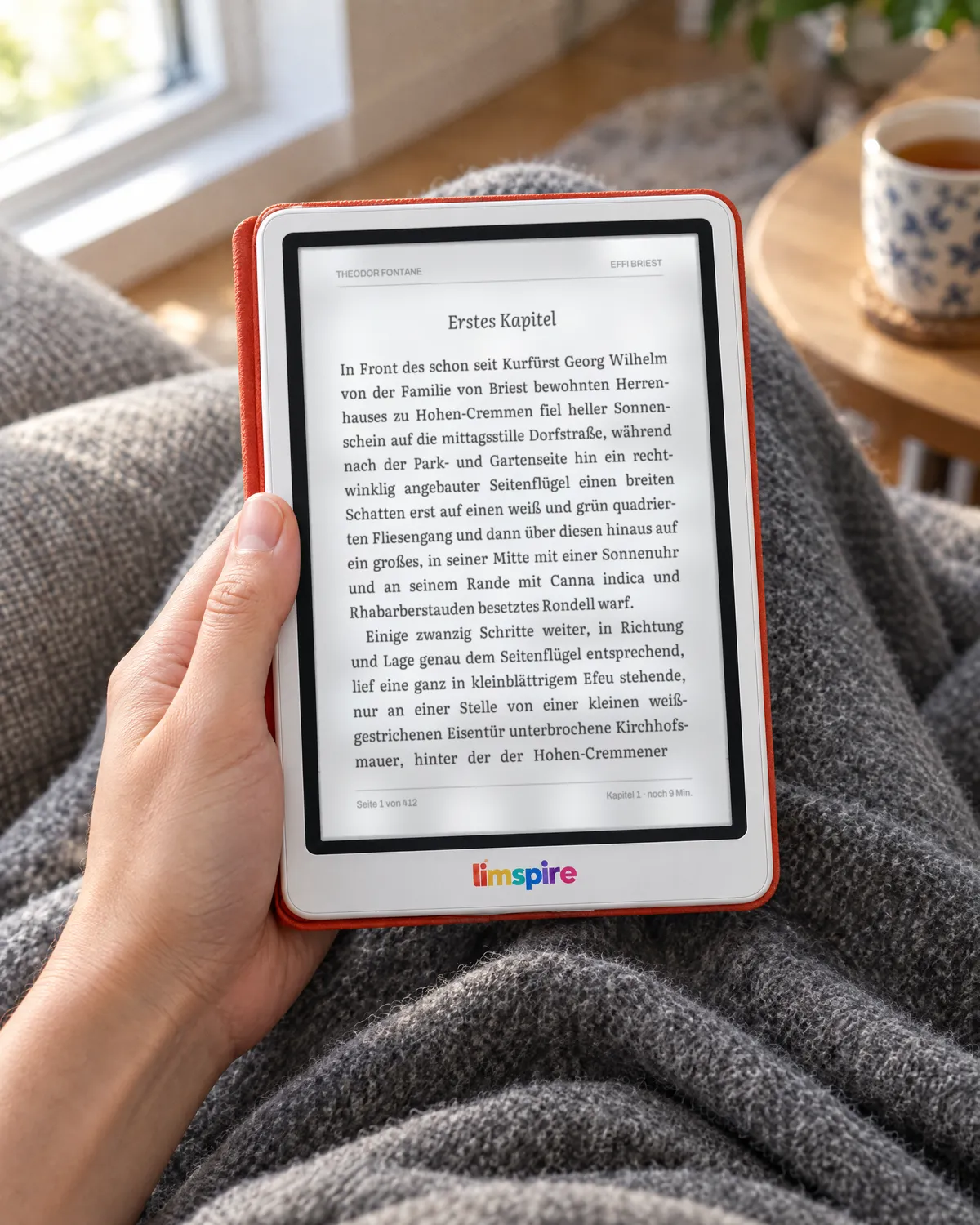 Eine Hand hält den limspire E-Reader in roter Hülle über einer grauen Wolldecke